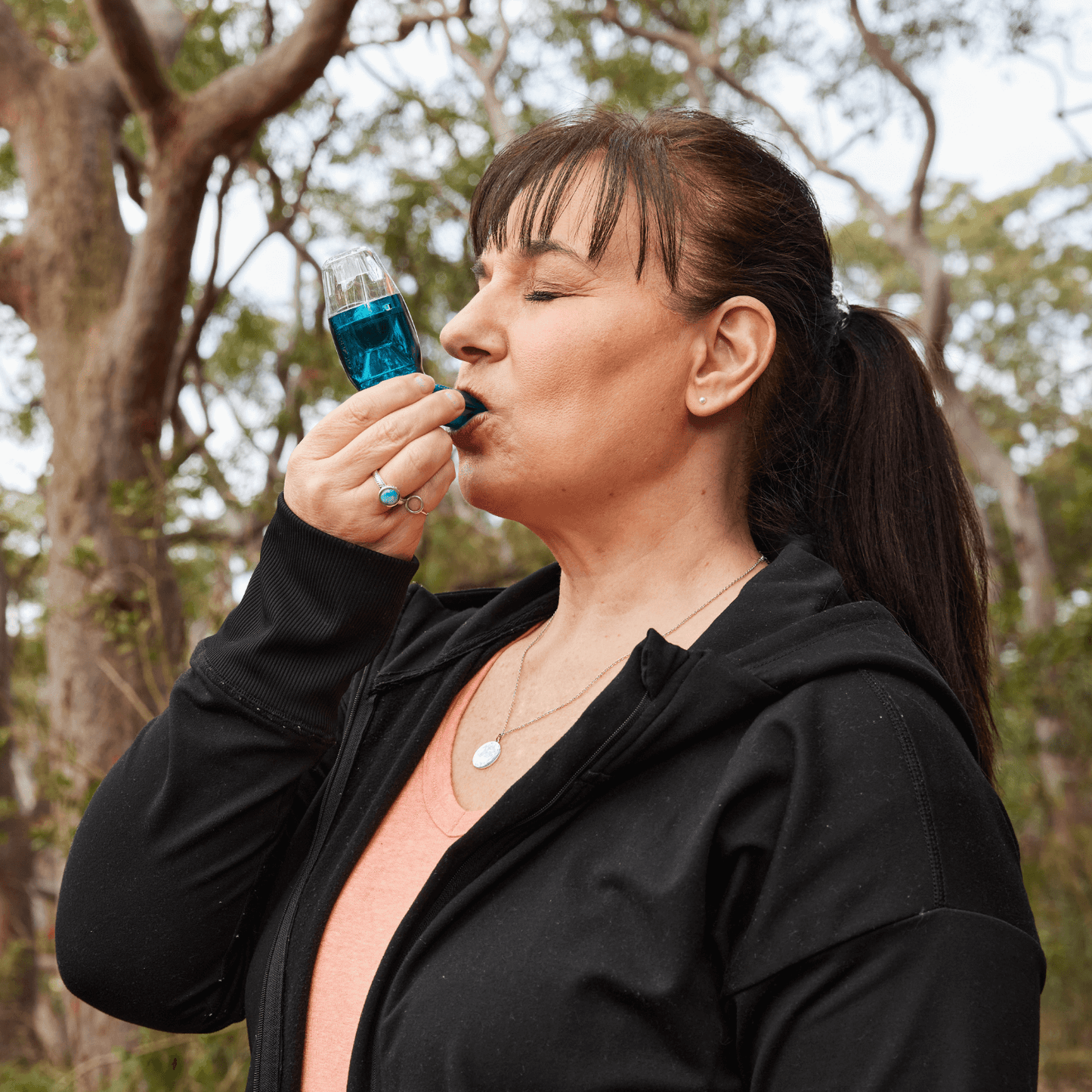 Woman who's wearing black sleeve tops using the blue breathing device with nature background