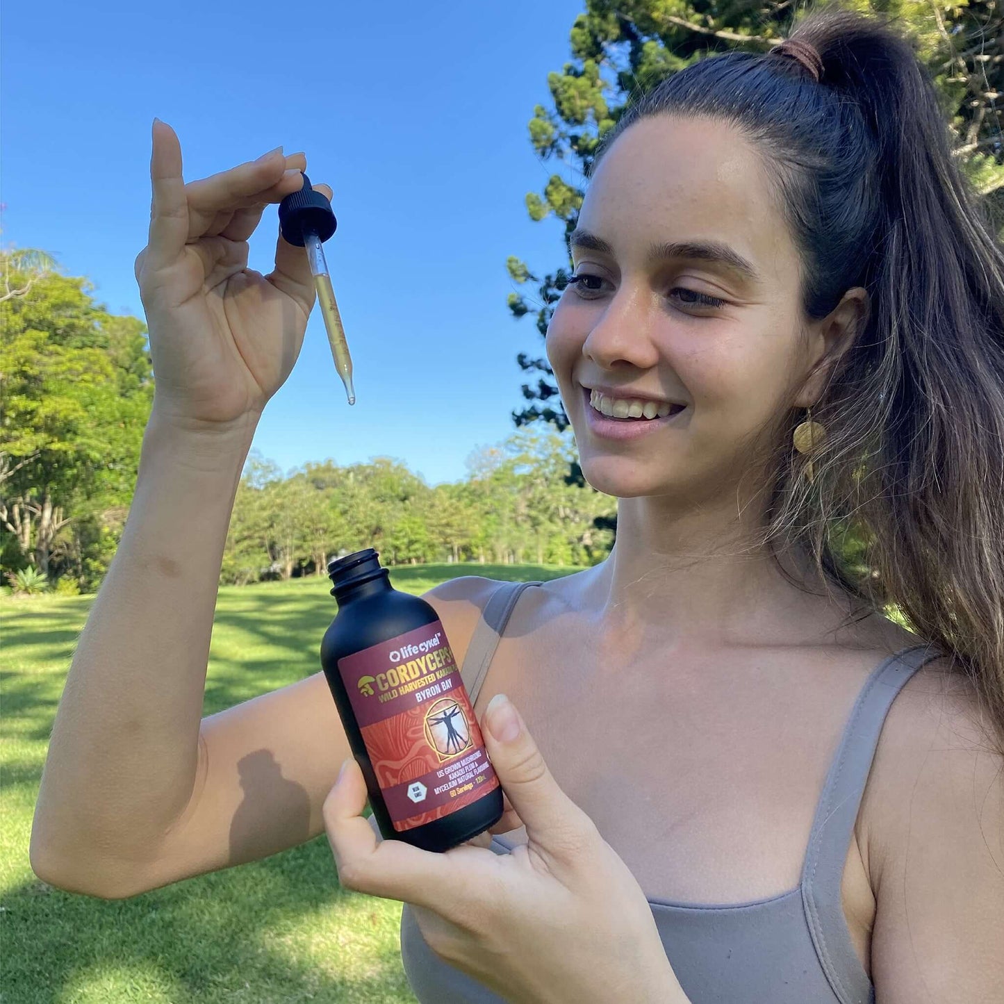 Woman wearing sports wear holding Lifecykel Cordyceps mushroom extract bottle with dropper