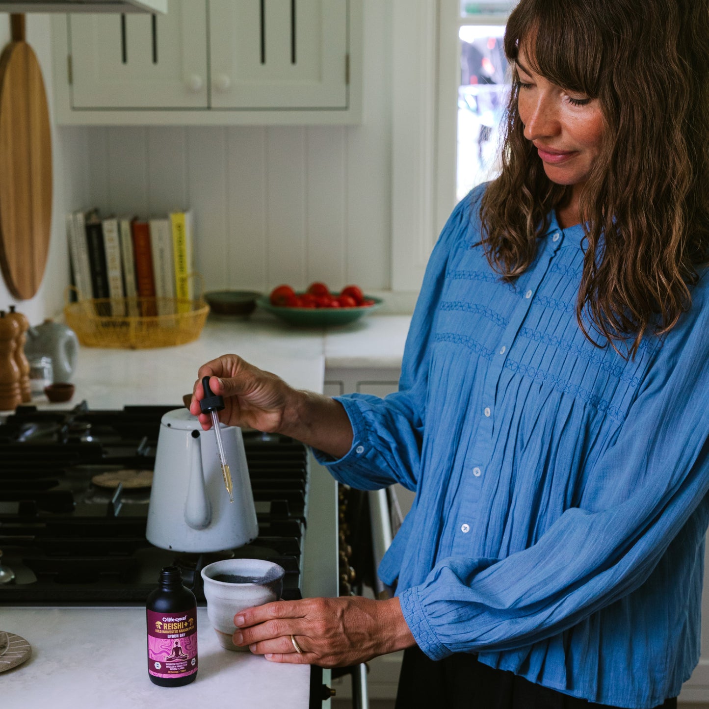 Woman in blue tops pouring a dropper of Lifecykel Reishi mushroom extracts on the ceramic cup.