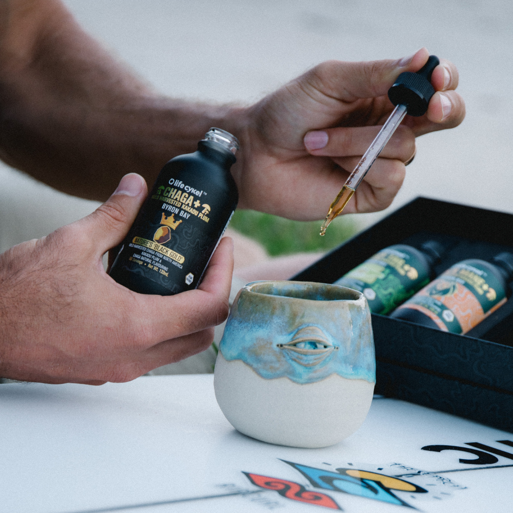 Person pouring a Lifecykel Chaga mushroom extracts from a dropper into a ceramic cup with a blurred background