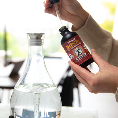Hand pouring a liquid from a bottle labeled 'Cordyceps' into a glass container.