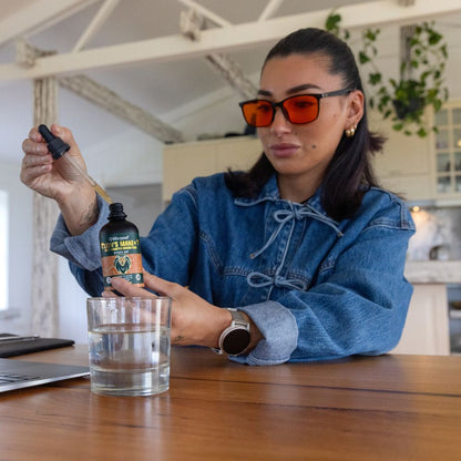 Person in a denim jacket and sunglasses pouring a Lifecykel Lion's Mane mushroom extracts liquid from a dropper bottle into a glass.