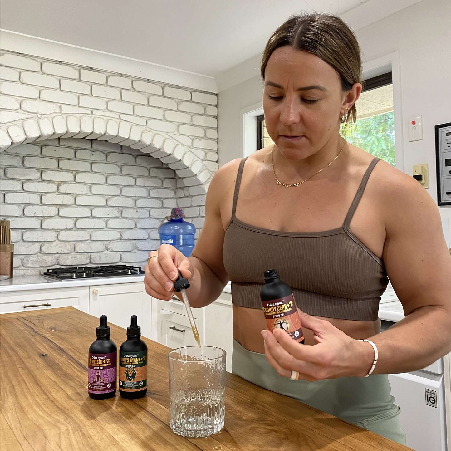 Athletic woman pouring a Lifecykel mushroom extracts liquid dropper on the glass cup of water.